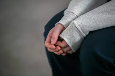 A young person sits with their hands held together.