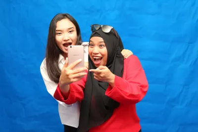  Two young women look into a mobile phone with big smiles.