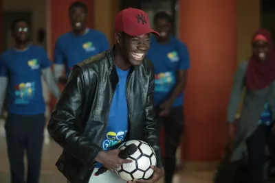 A young man holds a microphone and football as he laughs..