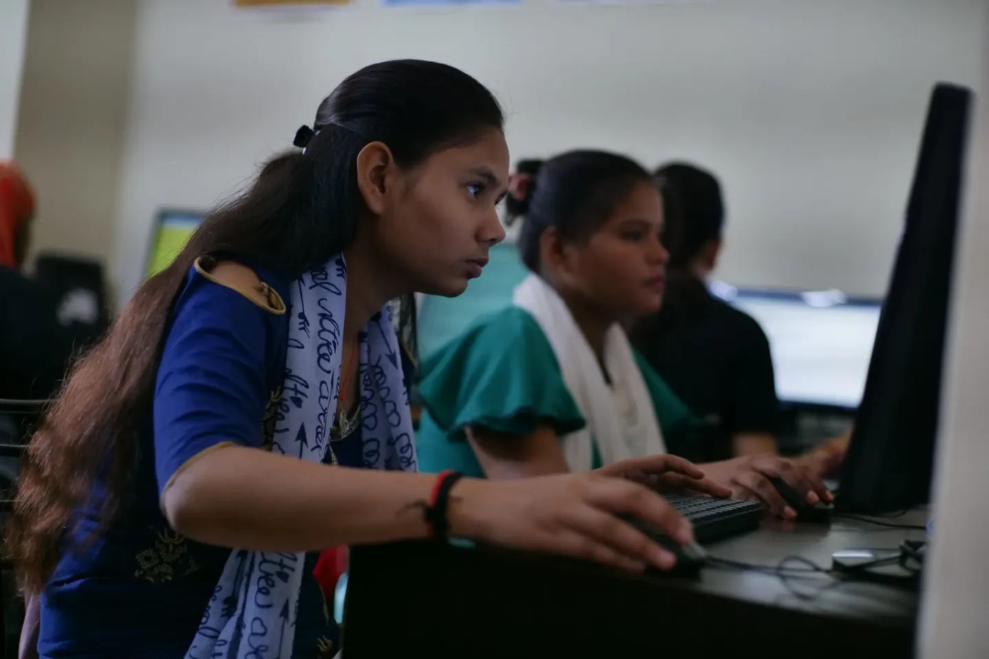 Young women working at desktop computers in a classroom or computer lab setting.