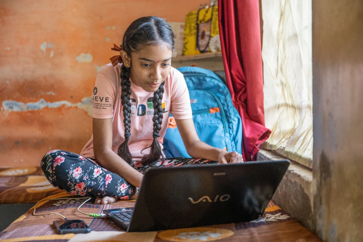 A girl is seated on the floor, focused on a laptop computer