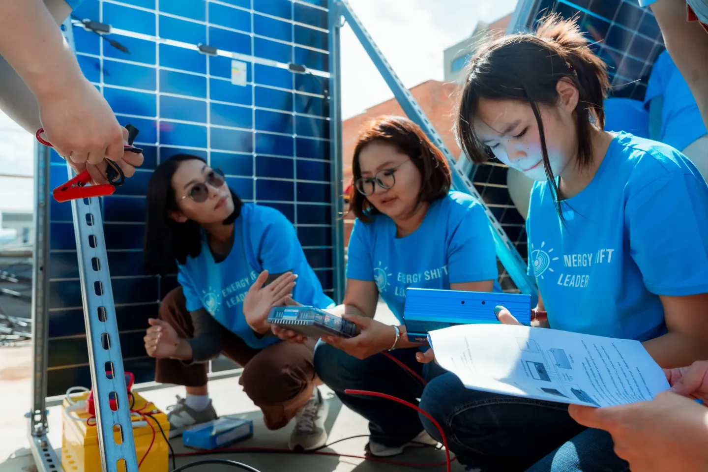 A group of young people from Mongolia in cyan blue T-shirts working together on activity, installing solar panels on a rooftop as part of a learning activity