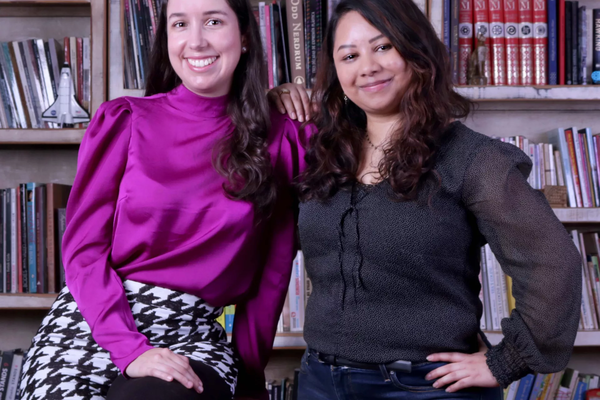 Andrea and Miroslava posing next to each other in front of a bookcase