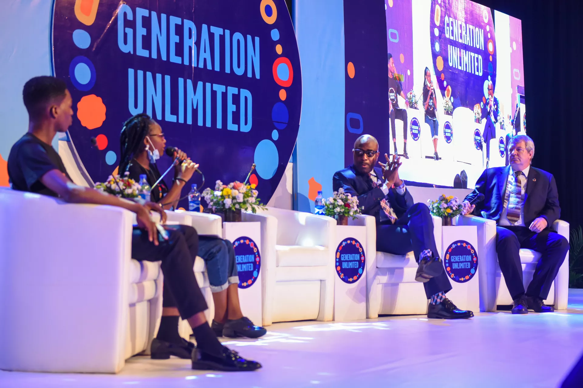 A group of young people shown in a panel discussion with decision-makers on stage