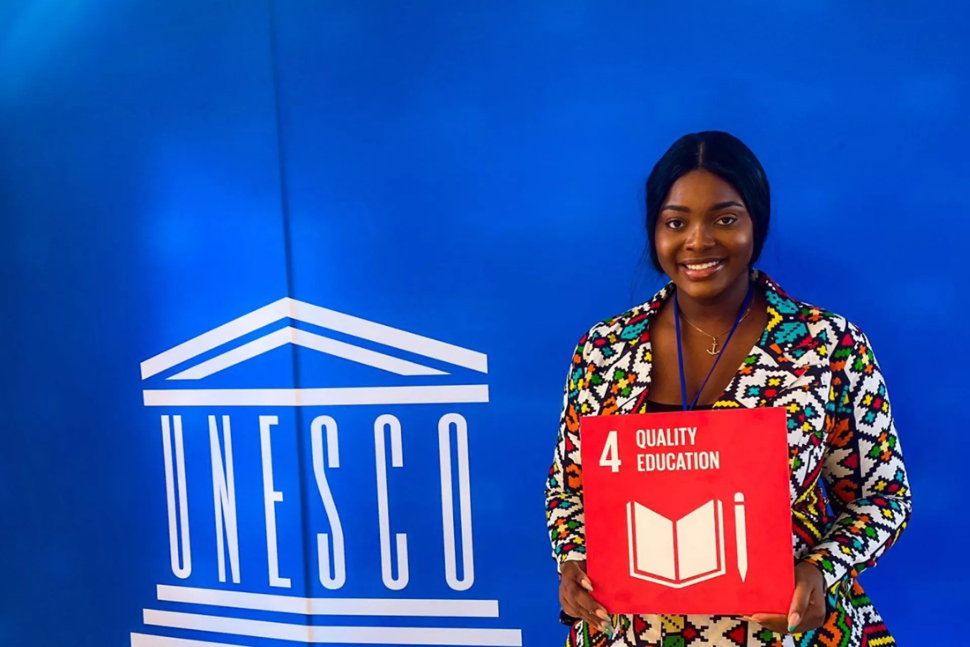 Precious Agaecheta holding an orange card for SD4 Quality Education in front of a UNESCO backdrop