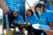 A group of young people from Mongolia in cyan blue T-shirts working together on activity, installing solar panels on a rooftop as part of a learning activity