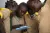 Four students crowd around a tablet, paying close attention in Camerooni.
