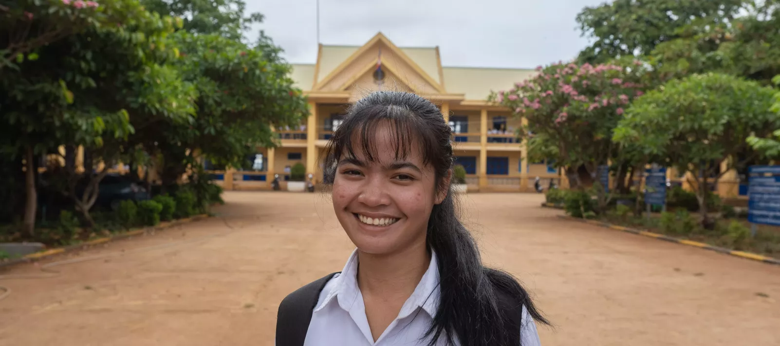 Channy Soy, 18, smiles brightly in front of her school. Channy is currently a grade 12 student and an indigenous ethnic minority scholarship recipient at Krong Banlung Boarding Secondary School, Thmar Da Village, Sangkat Beung Kansaeng, Banlung City, Ratanakiri Province. 
