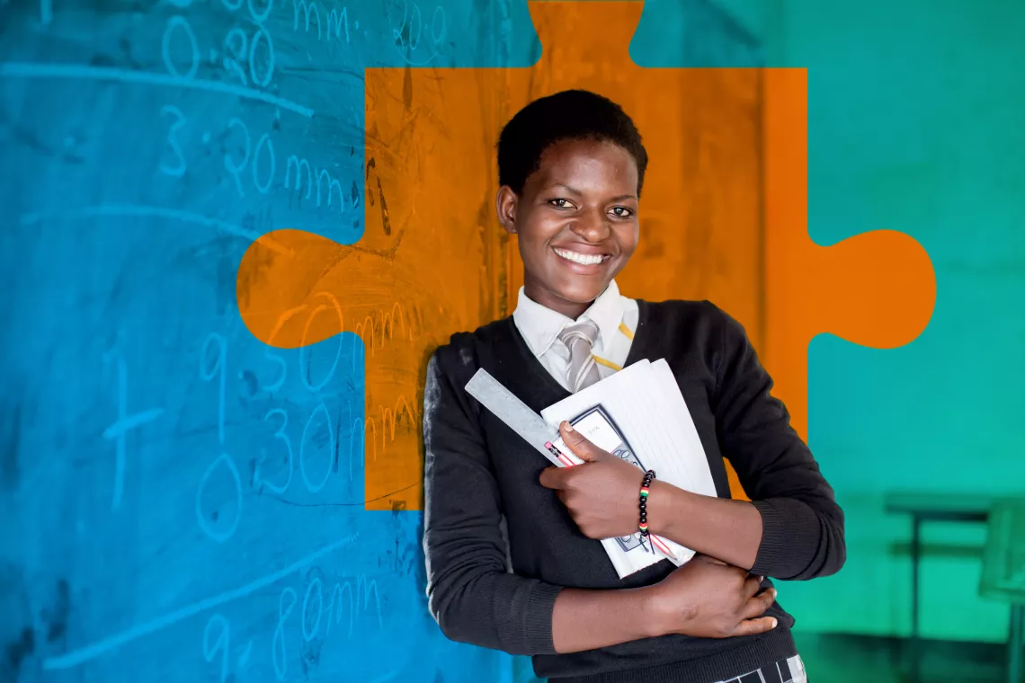 An adolescent girl leans against the blackboard, holding her school supplies, in a classroom in Zambia.