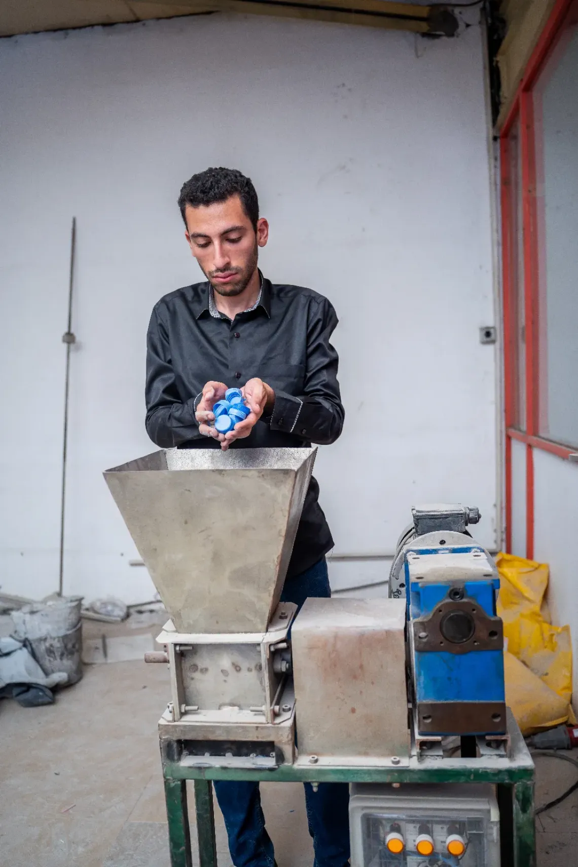 Ahmed, a young man from Egypt, shown operating a machine where he recycles plastic.