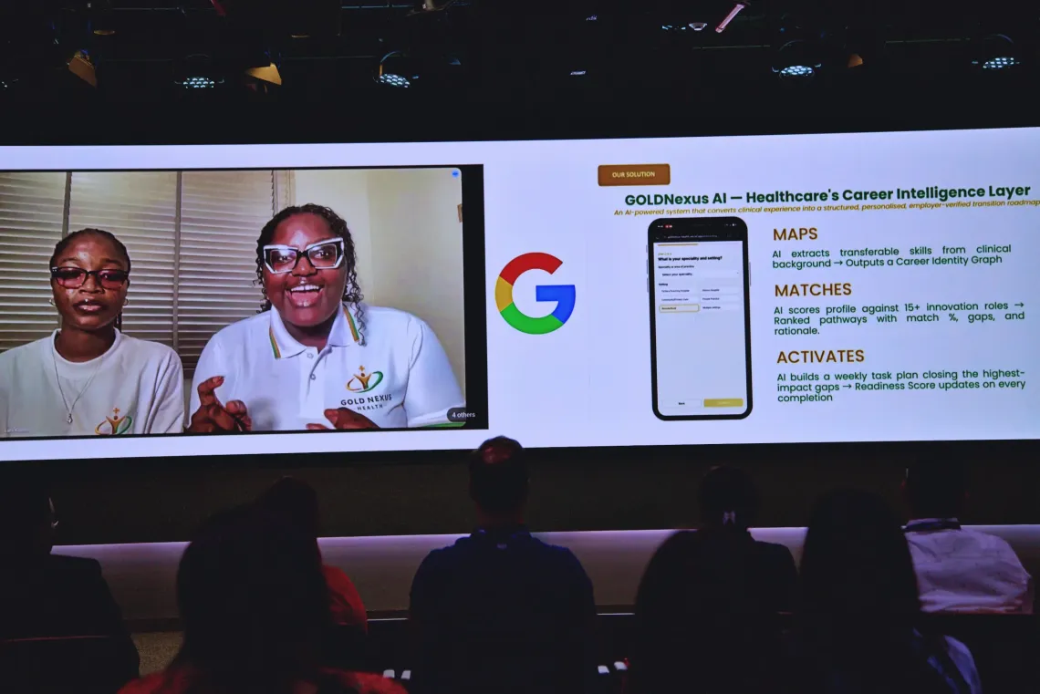 Large screen displays virtual speakers from Nigeria explaining the GOLDNexus Health solution. audience watches.