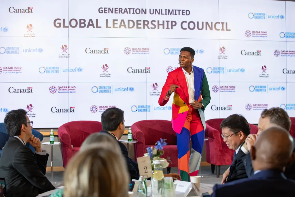 Spoken word poet Victory Ashaka speaking at a stage microphone in front of seated audience members at the Generation Unlimited Global Leadership Council event.