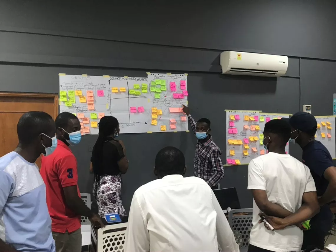 Picture of young people from Ghana gathered around a whiteboard laden with sticky notes