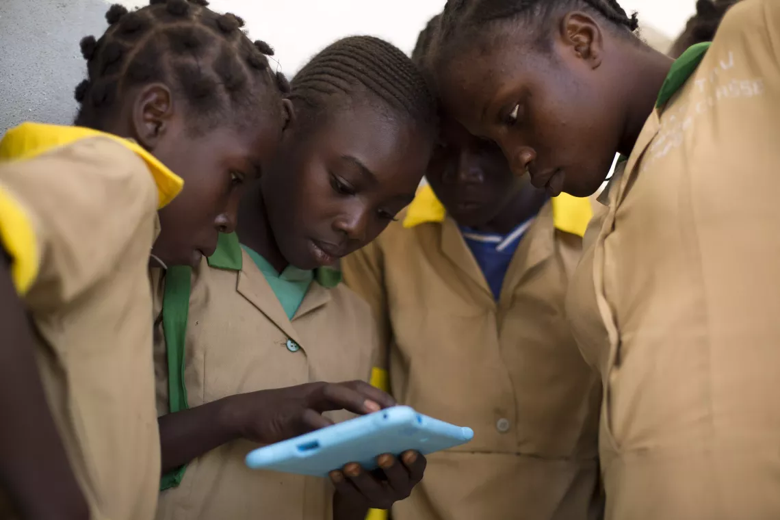 Four students crowd around a tablet, paying close attention in Camerooni.