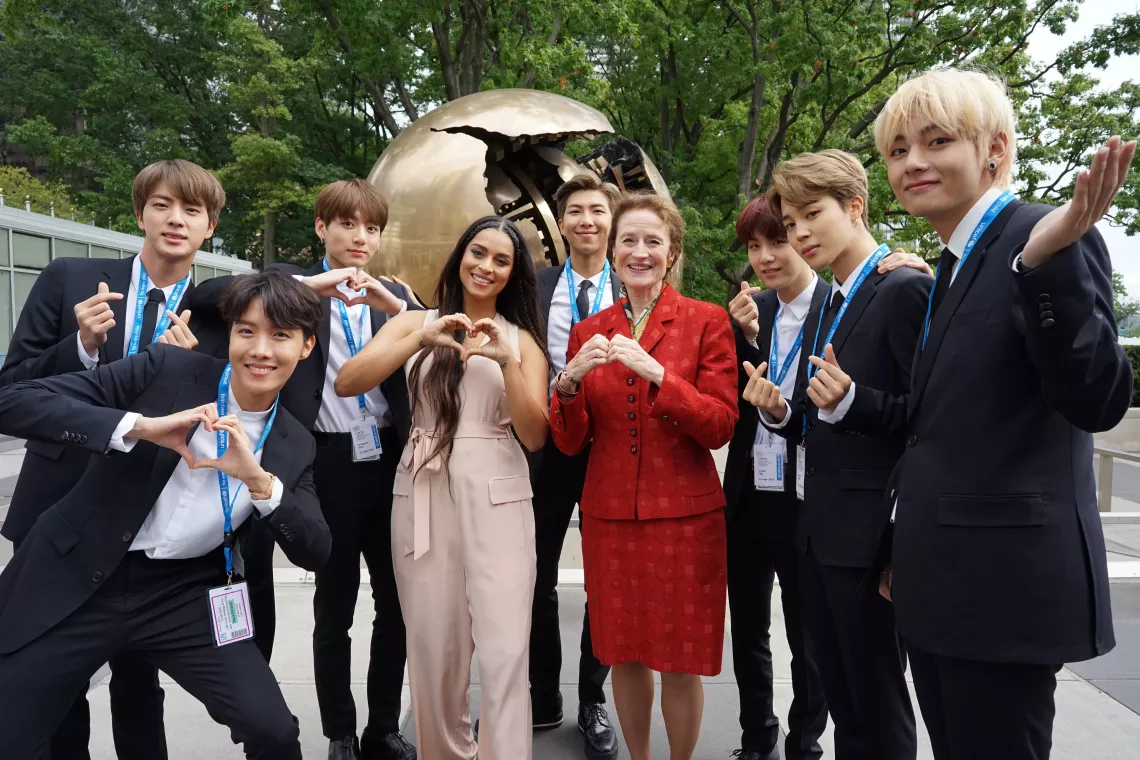Members of BTS make heart symbols with their hands, together with Lilly Singh and Henrietta Fore.