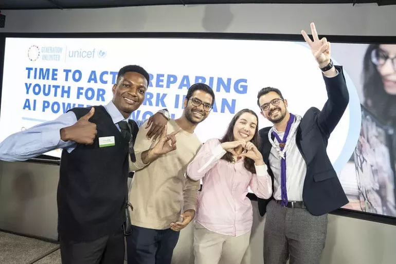 Four young people standing and smiling in from of a big screen 