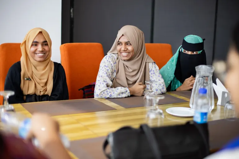 A group of young women in Bangladesh seated at a table smiling during a meeting.