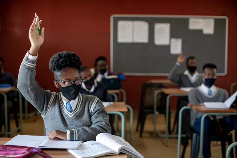 A young South African girl raises her hand in class
