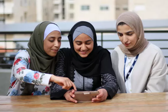Three young women sit together in Jordan, looking at a mobile phone.