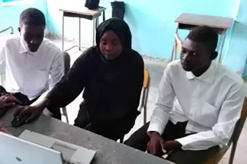 A team of three young people sits together at a computer.