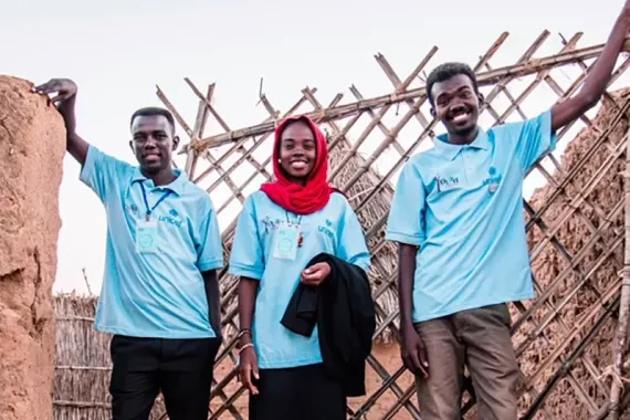 The Muntjatna team stands together outside by a fence, smiling.