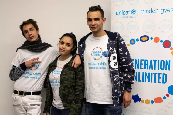 Three young people stand in front of a Generation Unlimited sign.