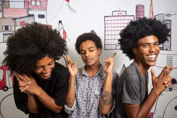 Three young people - members of Produção PRETA - laugh as they pose for a photo.
