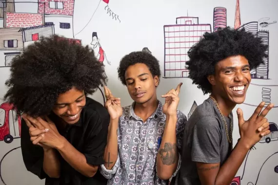 Three young people - members of Produ&ccedil;&atilde;o PRETA - laugh as they pose for a photo.