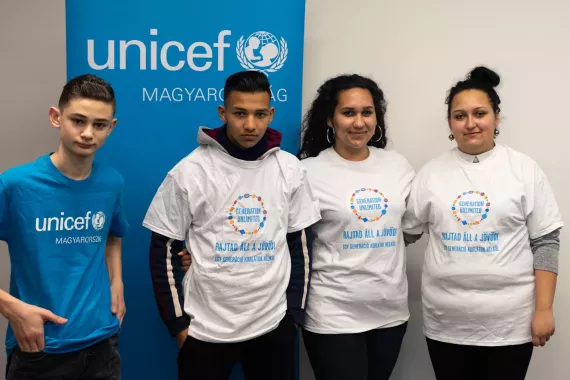Four young people stand in front of a UNICEF sign.