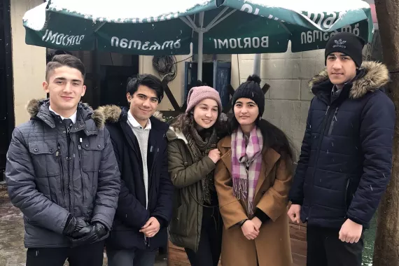 The five members of Youth Discovery stand together outside under a large umbrella, wearing warm winter clothes.
